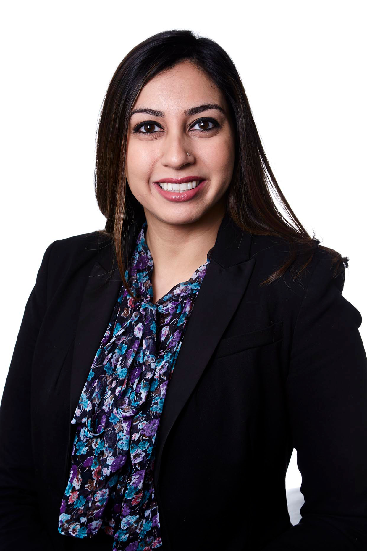 Smiling woman with long hair wearing a black blazer and a floral blouse on a white background.