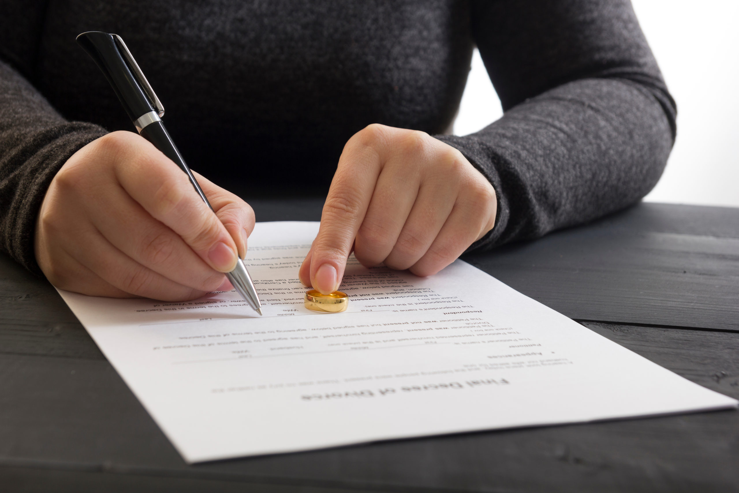 A person in a gray sweater signs a document labeled 