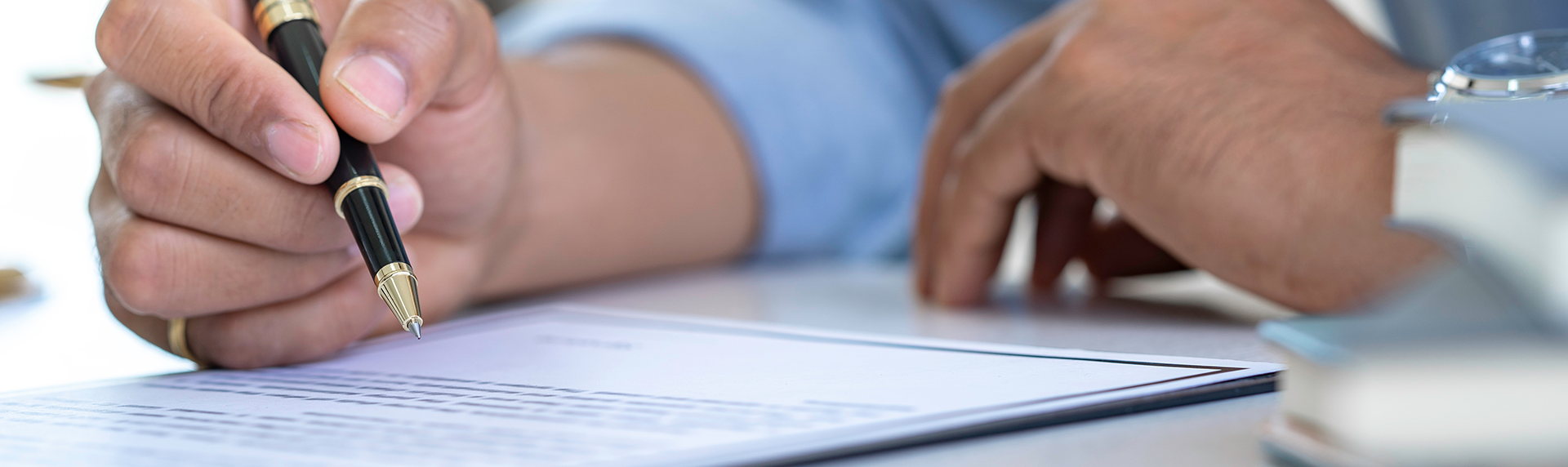 A criminal defense lawyer, wearing a crisp blue shirt, is poised to sign a document resting on the desk. Their watch gleams subtly as they prepare to add their signature, suggesting a pivotal moment in the legal process. Grounds For Divorce concept image