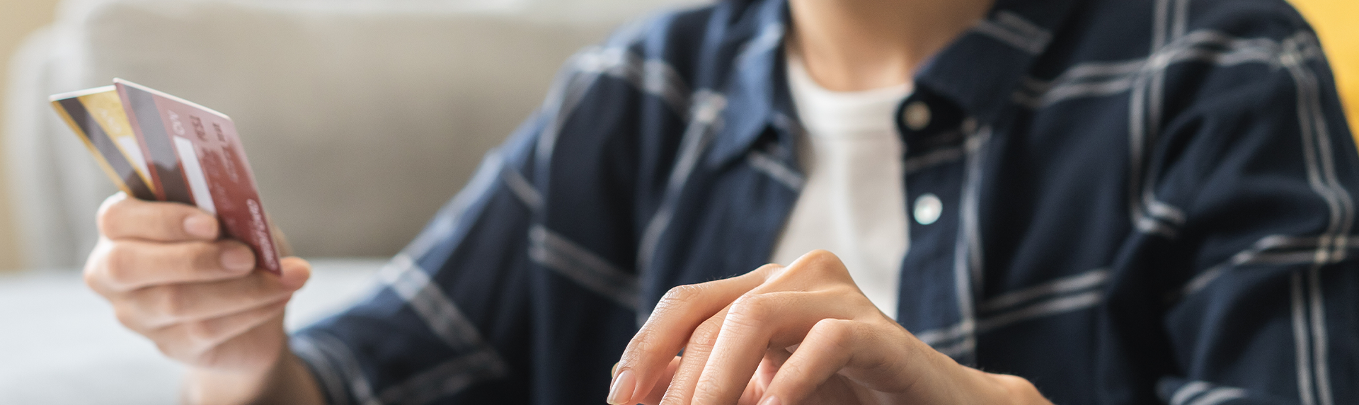 A person, perhaps a criminal defense lawyer, holds a credit card in one hand while typing on a laptop with the other. Dressed in a blue plaid shirt, they're seated at a table. The image captures the focus on their hands and card, hinting at diligent multitasking.