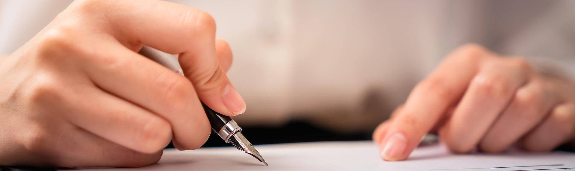A criminal defense lawyer is meticulously holding a black fountain pen, either writing or signing a crucial document. Their other hand, clad in a crisp white shirt, rests confidently on the paper. The background remains blurred, focusing all attention on this pivotal moment.