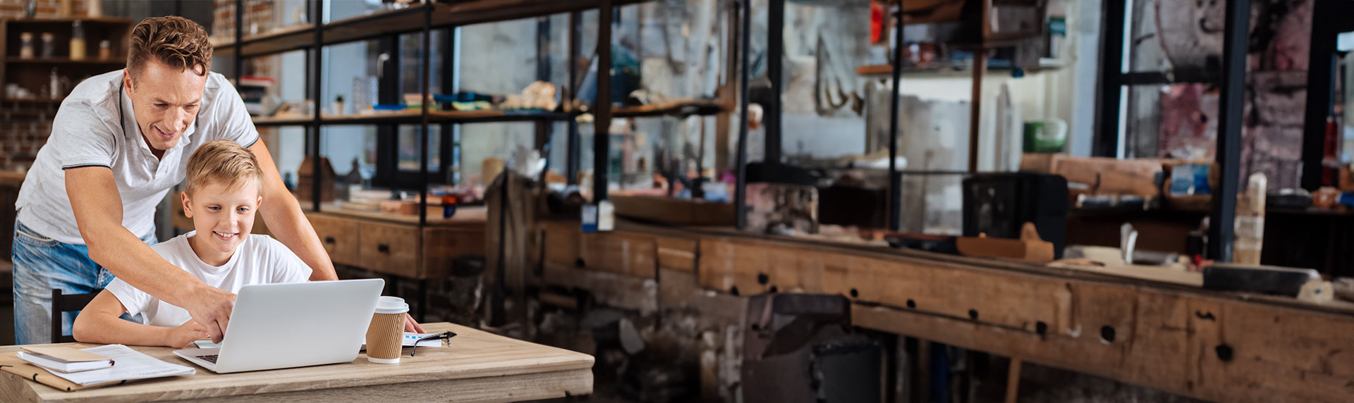 A man and a boy are happily looking at a laptop together in a workshop setting, where parental rights meet practical learning. They are surrounded by wooden workbenches and tools, creating an atmosphere that is casual yet focused on fulfilling learning obligations; Parental Rights Obligations attorney in Morristown NY concept image