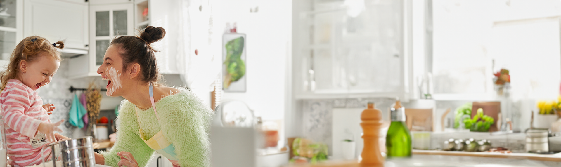 A woman and a young child, both sporting flour-dusted smiles, are enjoying a playful baking session in their bright kitchen. The child perches on the counter beside the mixing bowl and whisk. The room is flooded with light and plants abound, creating an atmosphere more inviting than a criminal defense lawyer's office.