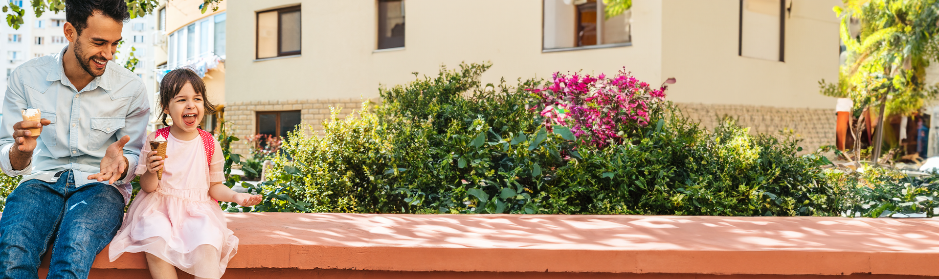 A man and a young girl enjoy ice cream while sitting on a low wall in a sunny garden, where vibrant flowers bloom in the background. Both are smiling and relaxed, perhaps savoring a rare moment away from his bustling work as a criminal defense lawyer; Child Support Modification Attorneys in Morris County concept image