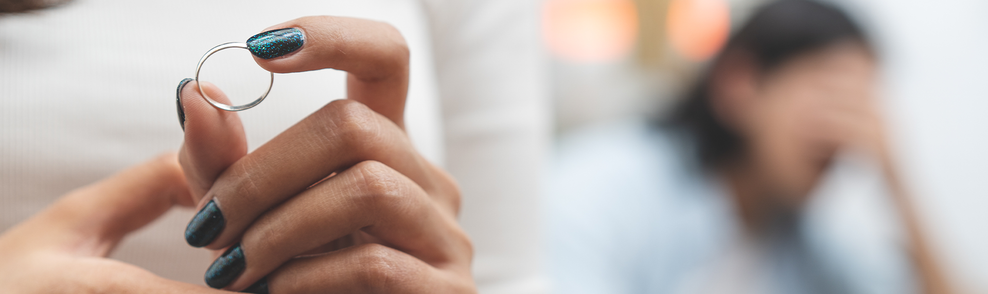 A person with glittery teal nail polish holds a ring in focus. In the blurred background, a Criminal Defense Lawyer appears upset, with their hand covering their face. The scene suggests an emotional context.