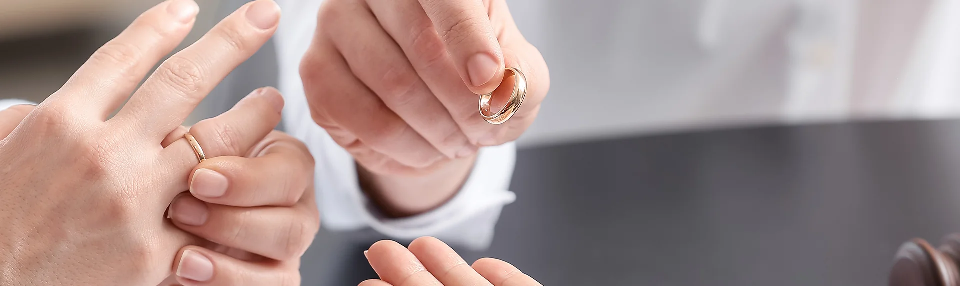 Two hands exchanging rings over a dark surface evoke a sense of commitment, like forging an unbreakable bond. One person is slipping on a ring as the other holds another between their fingers, reminiscent of how a criminal defense lawyer steadfastly defends their client. Both wear white outfits.