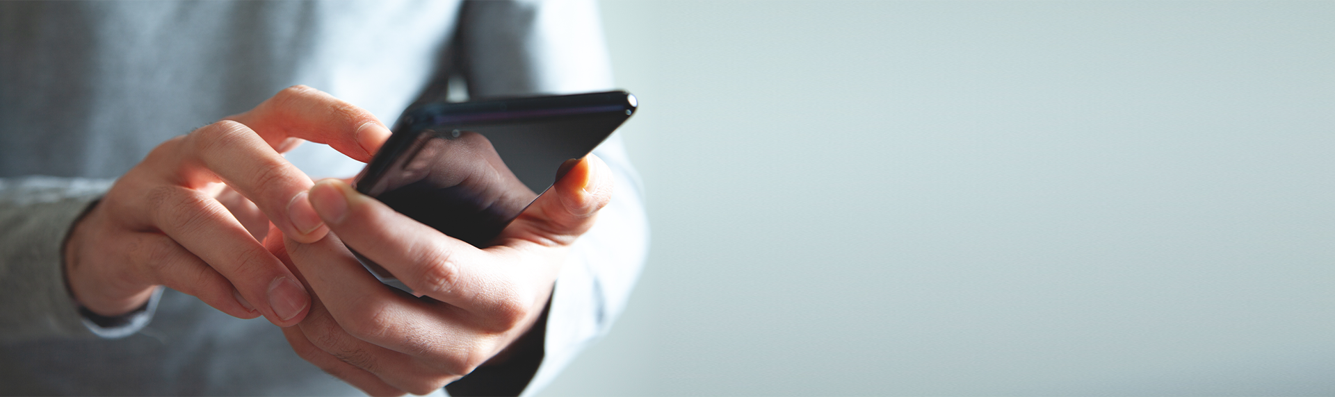 A criminal defense lawyer deftly navigates their smartphone, fingers expertly gliding across the screen. The blurred, neutral background shifts focus to their hands and the device, seamlessly integrating into their professional attire of a long-sleeved shirt.