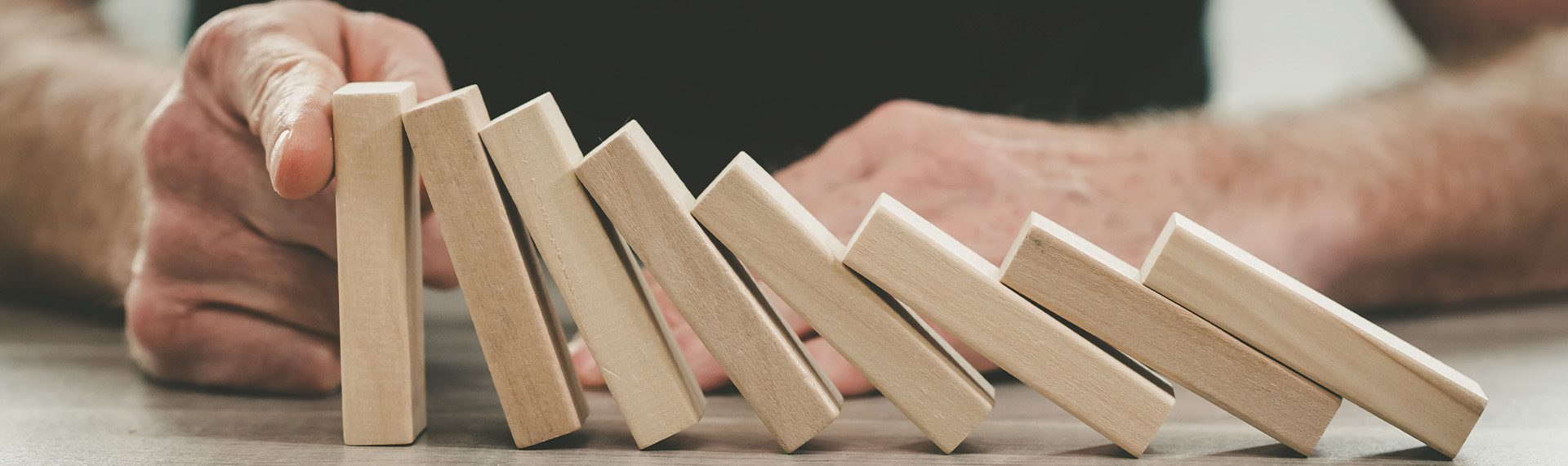 A hand suddenly intervenes, stopping a line of wooden dominoes from toppling over on a smooth surface. This act of prevention is much like hiding assets—strategically halting a chain reaction before its inevitable cascade.
