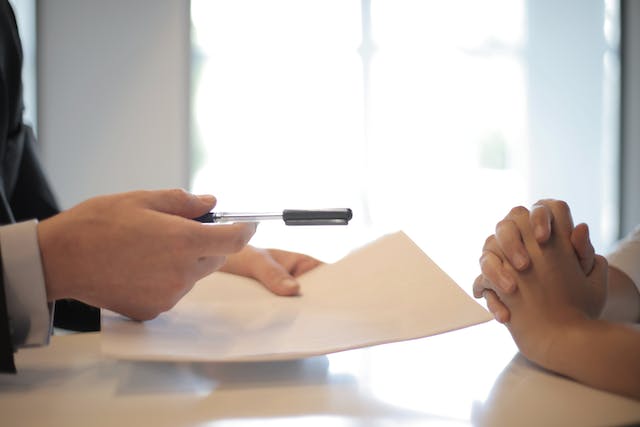 person handing paper and pen to someone else