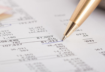 A close-up of a gold pen pointing to a highlighted number on a financial affidavit divorce document, surrounded by rows of numerical data and figures.