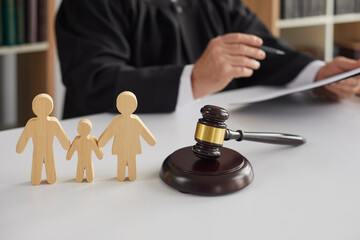 A judge reviews documents at a desk with a gavel and three wooden cutout figures symbolizing a family, illustrating the legal process when parties seek to modify custody without court intervention.