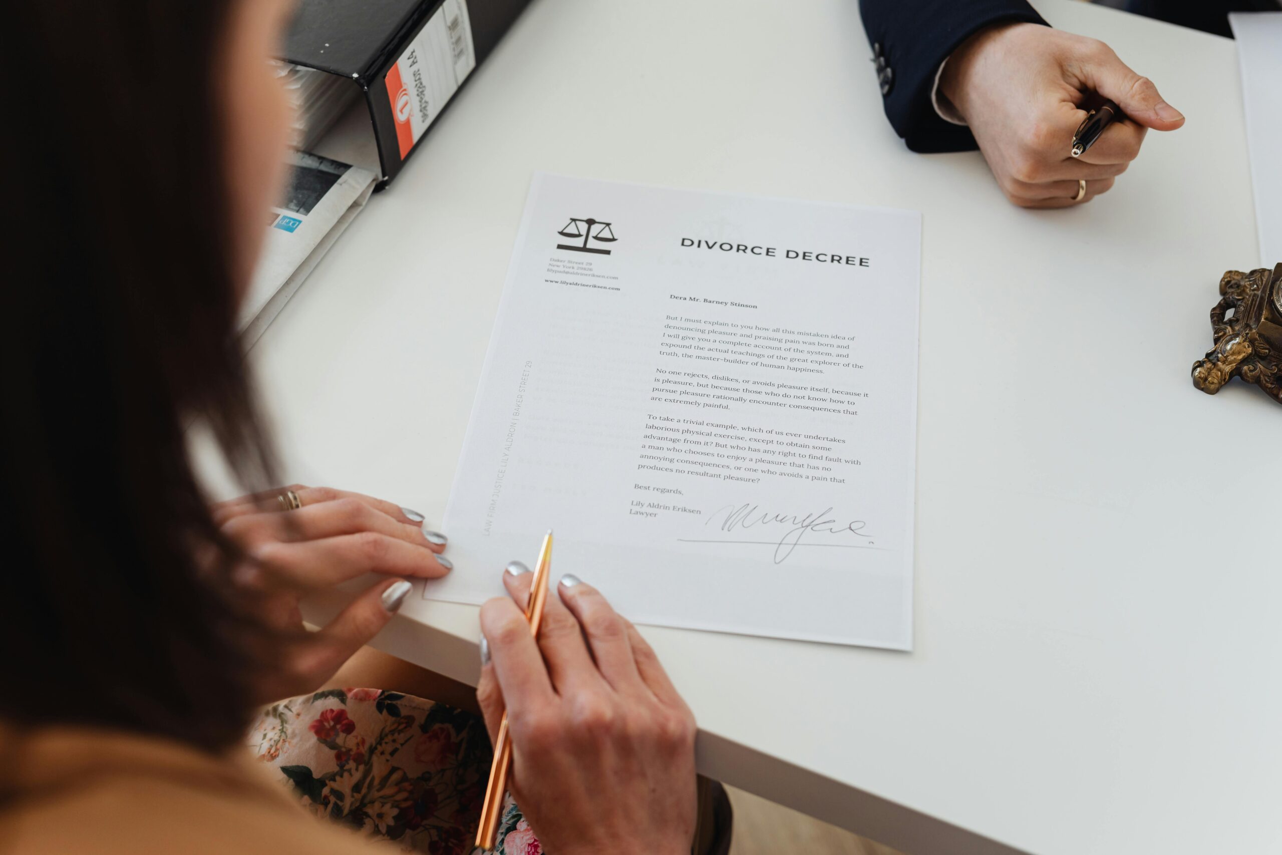 A person holding a pen reviews and prepares to sign New Jersey divorce papers on a white table, while another person sits across from them, also holding a pen.